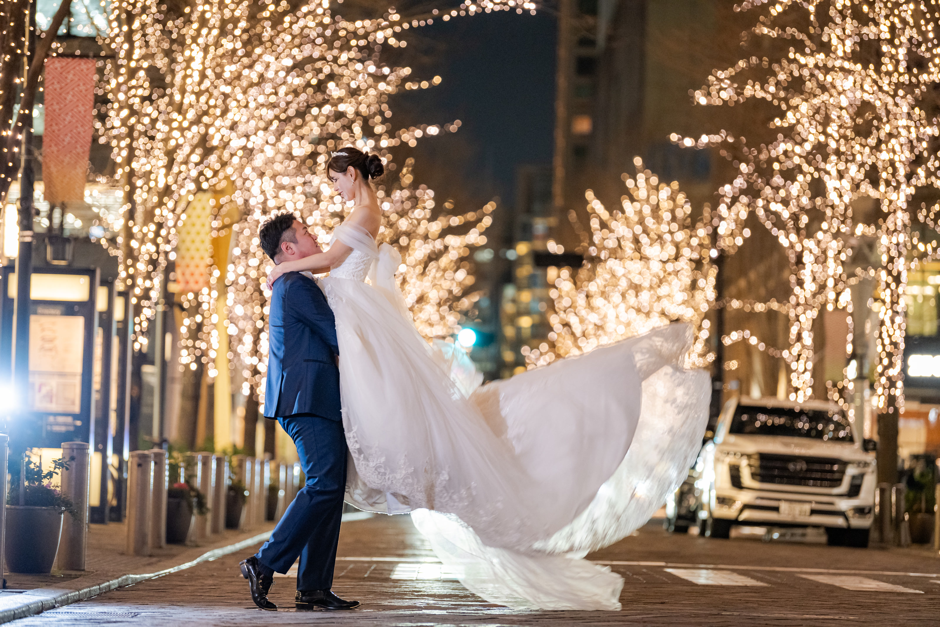 Groom lifting his bride beneath winter illuminations, a frame from a pre-wedding film