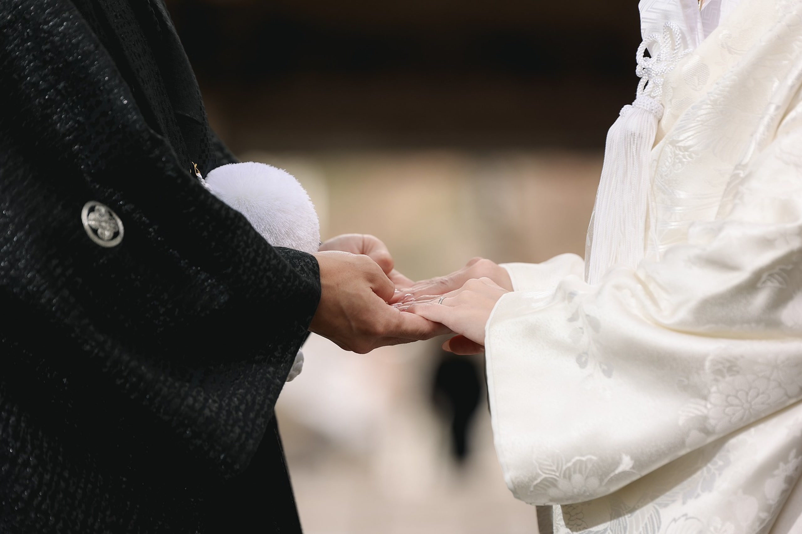 Hands of a couple in shiromuku and montsuki kimono, held together in close detail