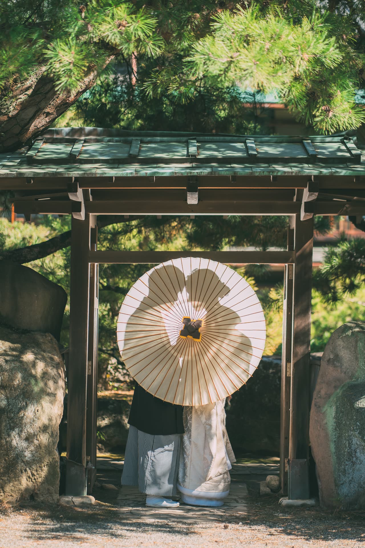 新人以和傘遮住身影,站在庭園木門下的日本婚紗攝影