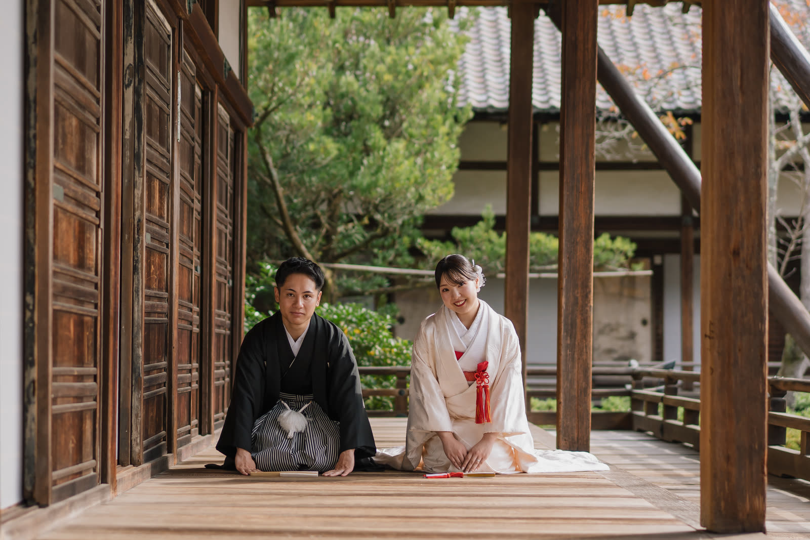Couple in kimono seated side by side on a wooden engawa veranda looking out over a Kyoto garden