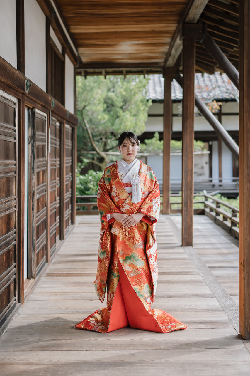 Bride in a red iro-uchikake kimono standing in a wooden temple corridor in Kyoto