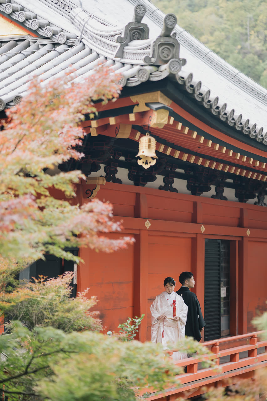 Couple in traditional kimono before a vermilion temple gate seen through autumn maple leaves in Kyoto