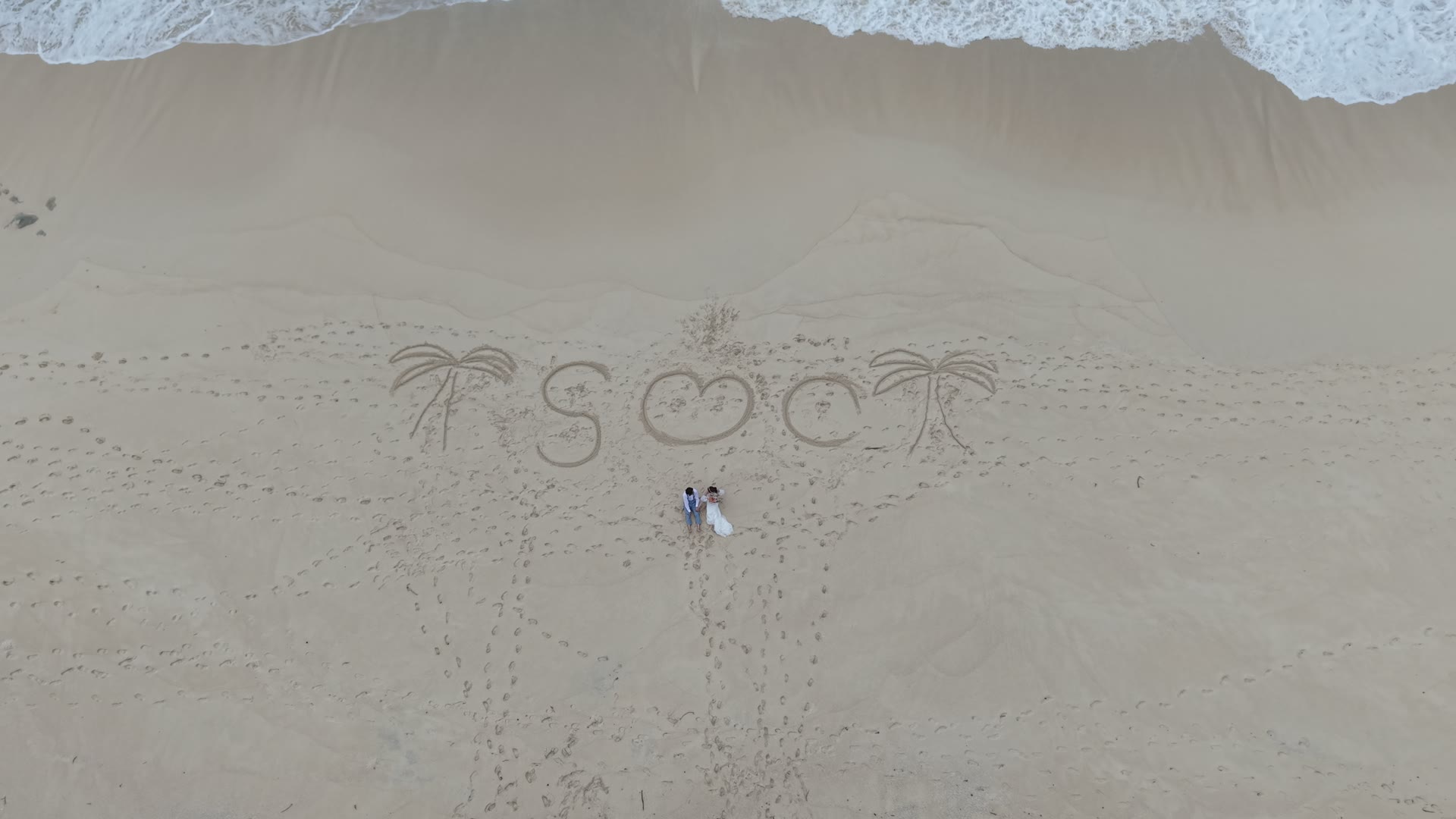 沖繩白沙海灘的空拍畫面，新人身旁的沙上畫著愛心，日本婚紗攝影
