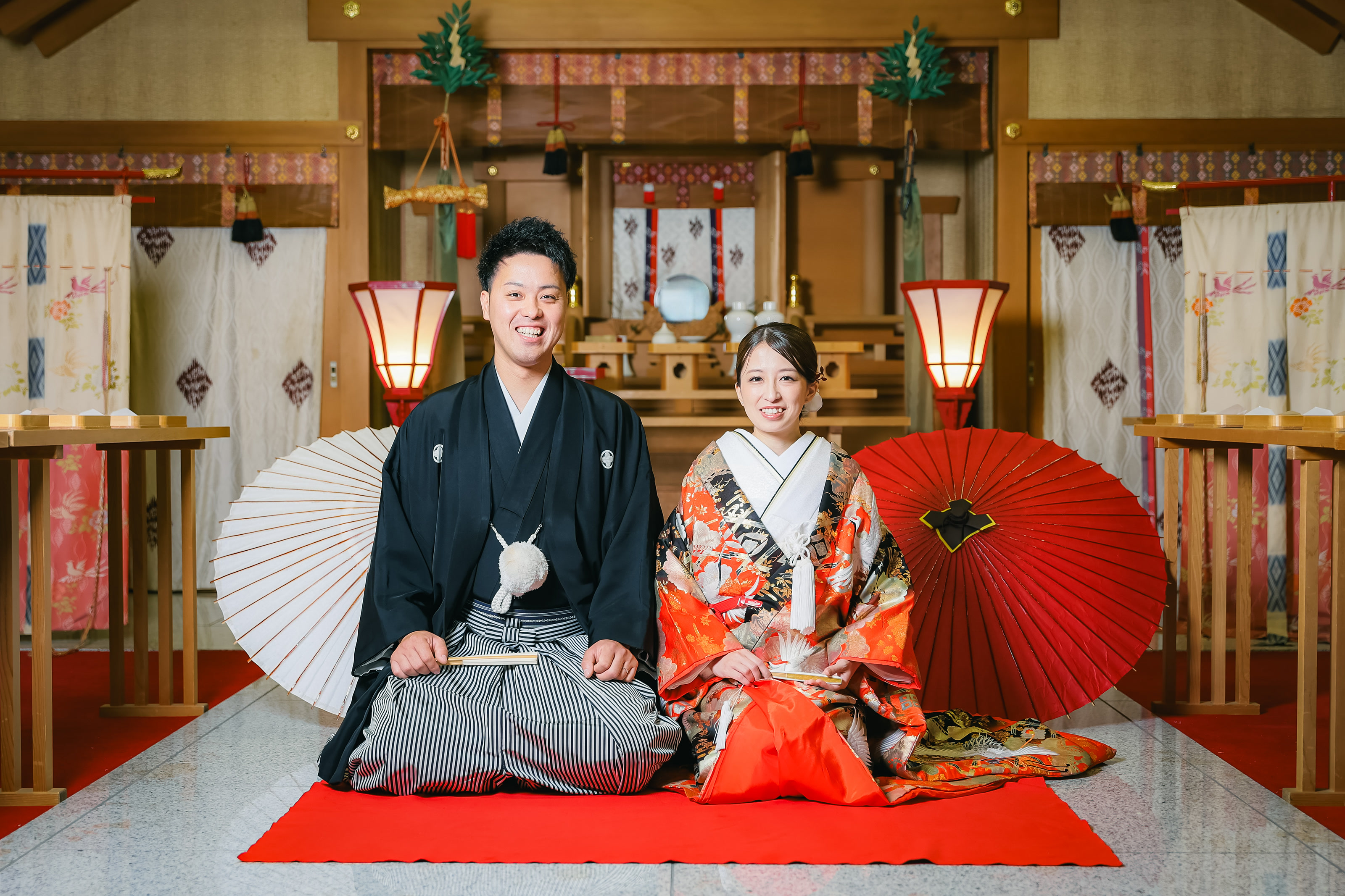 Couple seated in formal kimono with paper umbrellas inside a Shinto shrine hall