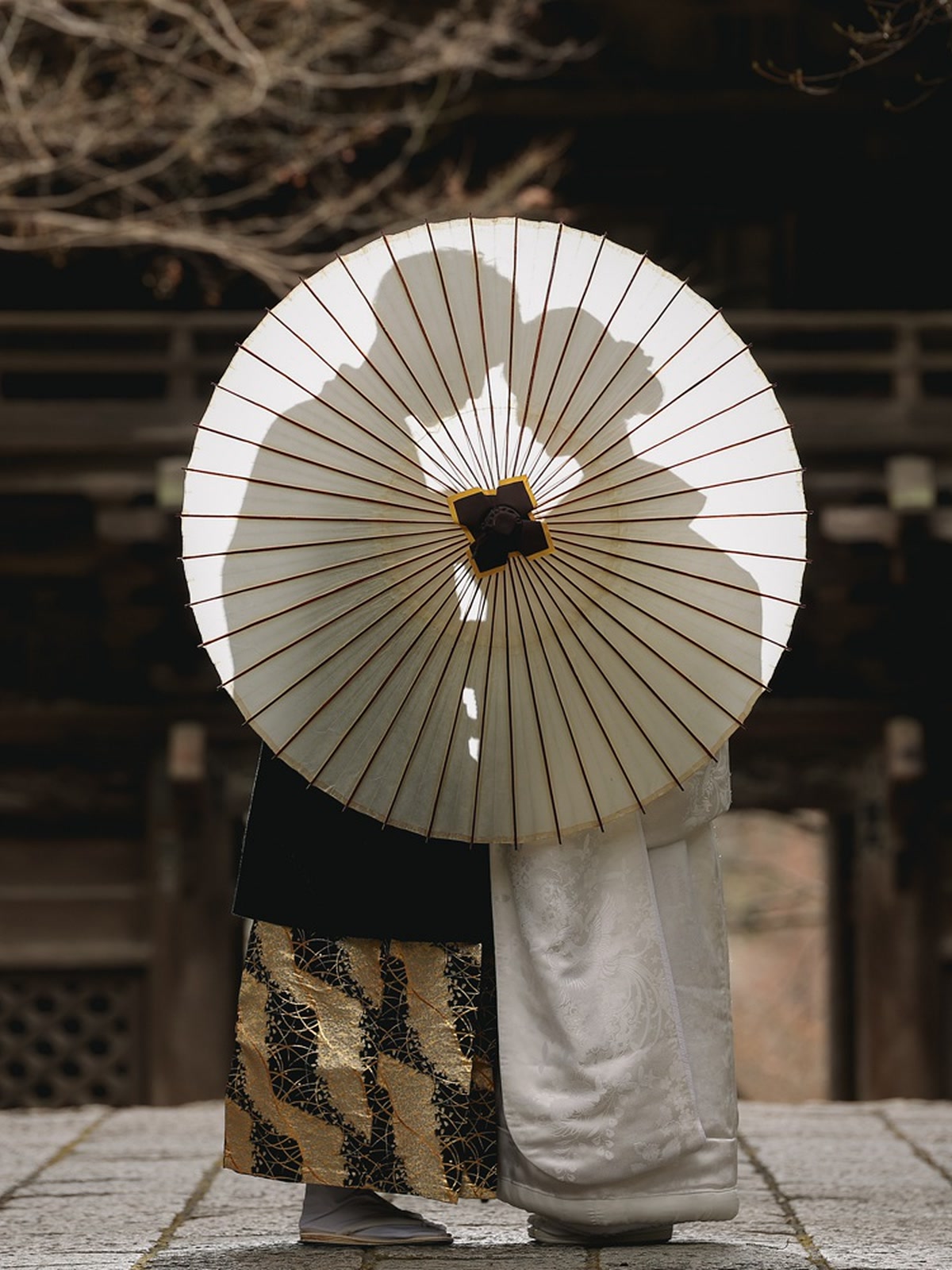 Couple in kimono sharing a paper umbrella on a lantern-lit shrine path at night