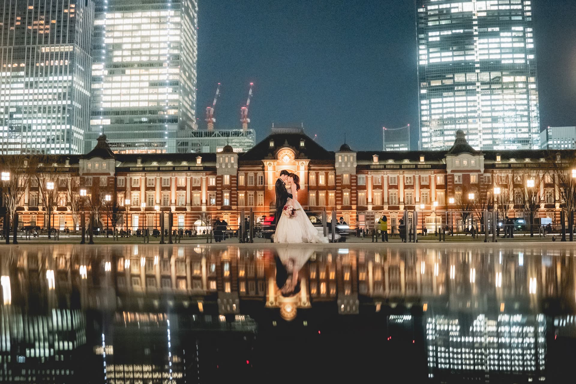 新人於夜晚的東京車站紅磚建築前拍攝,倒影映在水面上