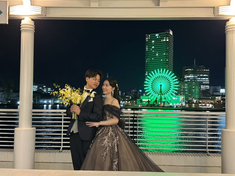 夜晚的露台上,新人身後是燈光閃耀的港灣與摩天輪